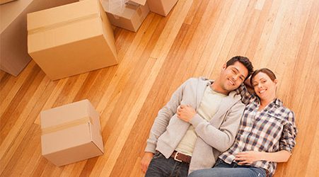 A man and woman take a moment to relax on the floor while packing up their belongings into cardboard boxes.